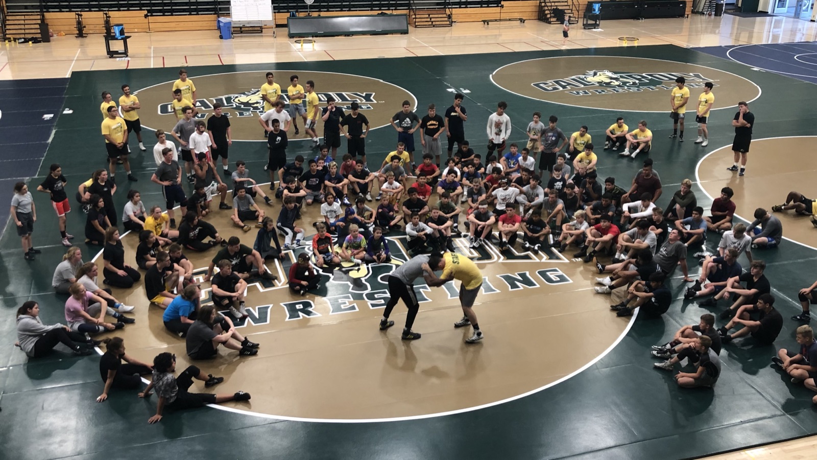 Campers and coaches huddled at center mat during a team talk at the Cal Poly wrestling facility