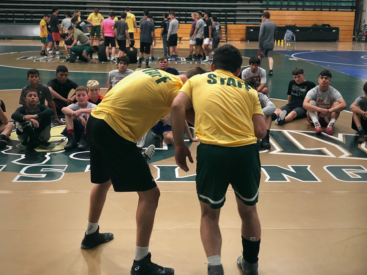 Two staff members in STAFF shirts demonstrate a position for campers